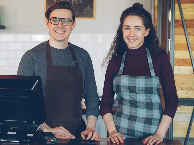 Deux commerçants souriants derrière le comptoir de leur café